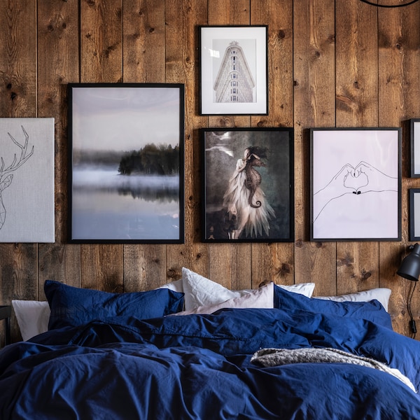 A bedroom with a bed with blue bed linen and framed nature-inspired artwork on a rustic wooden wall.