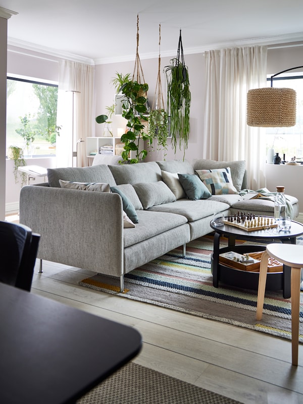 A beige/brown SÖDERHAMN sofa with hanging plants above and a black BORGEBY coffee table with a game and bottle on top.