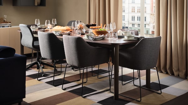 A beige living room with a STRANDTORP extendable table set for dinner surrounded by TOSSBERG and LÅNGFJÄLL chairs.