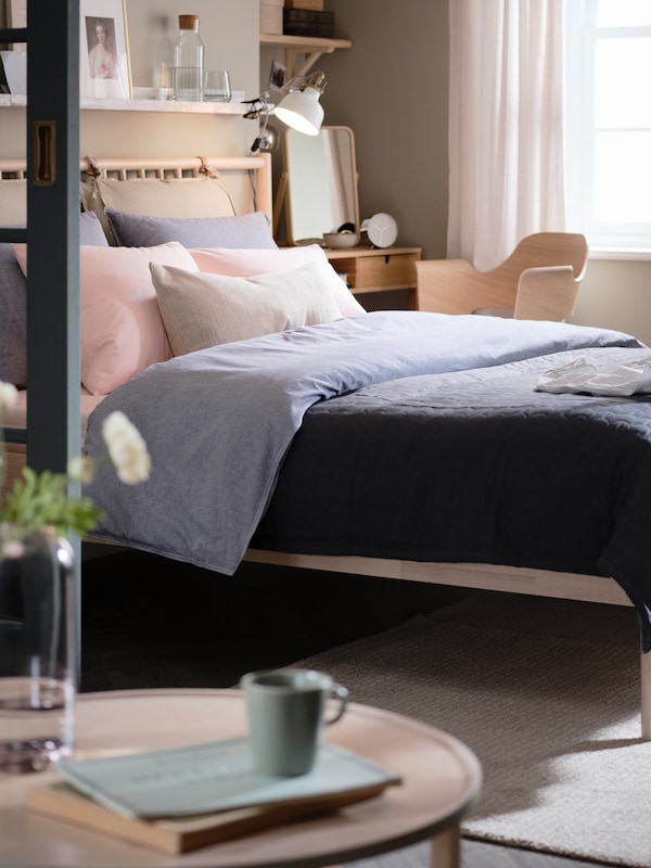 A birch BJÖRKSNÄS bed with a duvet in a dark blue KOPPARBLAD duvet cover stands in a bedroom near a window.