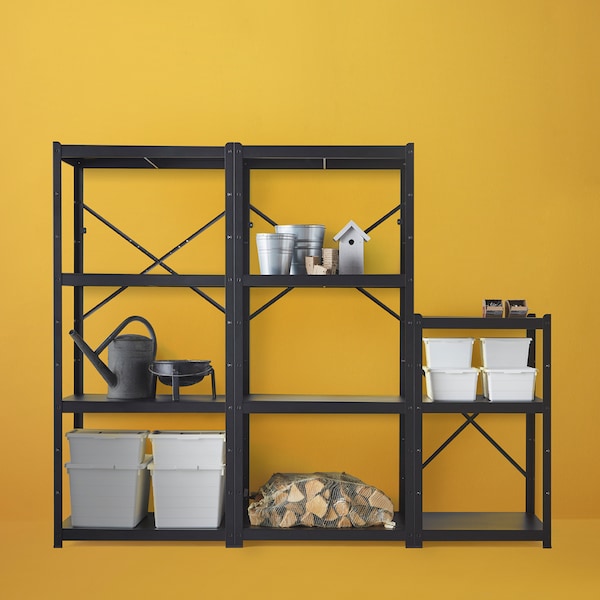 A black BROR shelving unit combination against a light orange wall, with firewood, white storage boxes and gardening items.