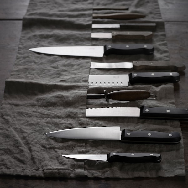 A black fabric knife holder rolled out flat with about 10 knives in it. Some are inside the pocket, others are on top.