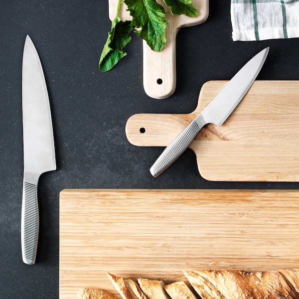 A black surface holding three wooden chopping boards and two kitchen knives. A loaf of bread is on one chopping board.