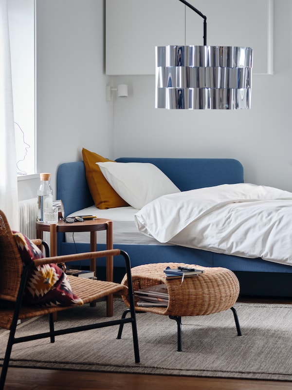A BLÅKULLEN upholstered bed with corner headboard and ÄNGSLILJA bed linen stands in a corner of a bedroom.