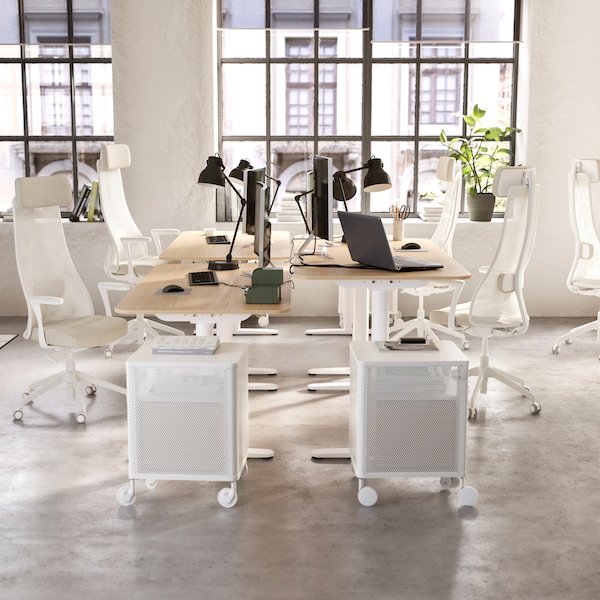 A bright open plan office with four BEKANT desks in a cluster each with a white office chair and black work lamp.