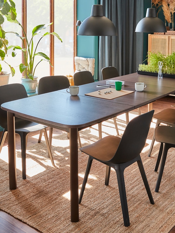 A brown STRANDTORP extendable table, anthracite ODGER chairs, two black pendant lamps and large windows.