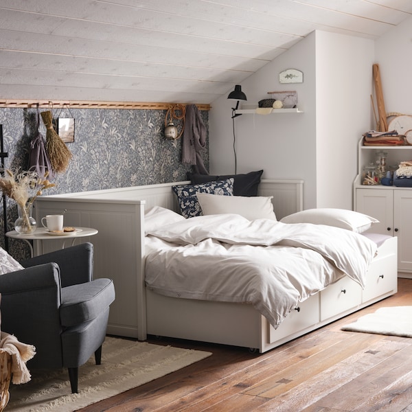 A cozy bedroom with a slanted roof, white daybed with three drawers, and a white HAUGA cabinet with 2 doors.
