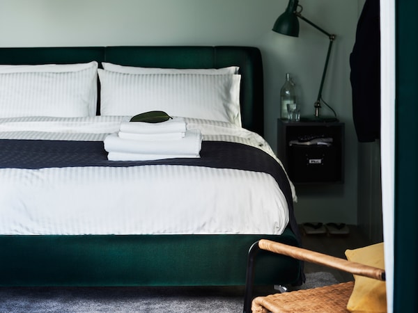 A dark-green TUFJORD upholstered bed with NATTJASMIN bed linen stands in a bedroom against a green wall.