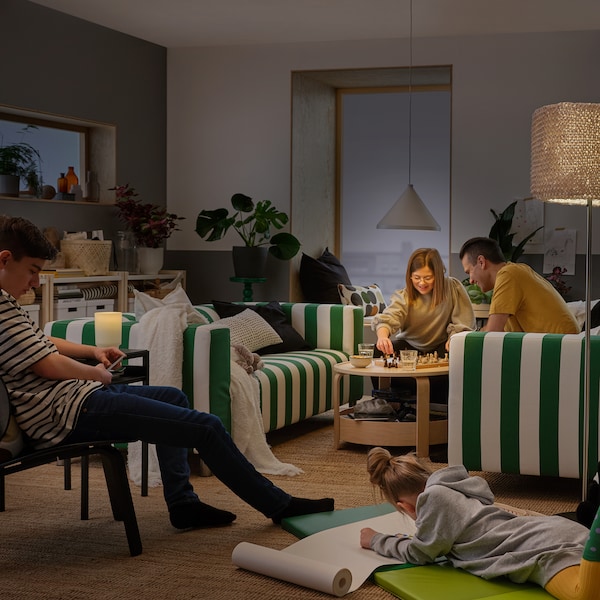 A family relax in their living room which is lit by a NÄVLINGE pendant lamp, an ISBRYTARE table lamp and a floor lamp.