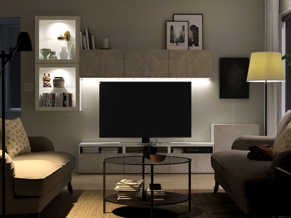 A flat screen TV on a gray TV stand with sofas in front.