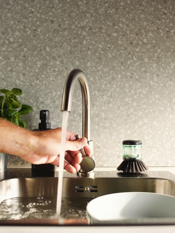 A hand turning off a kitchen faucet which is filling a sink with dishes.