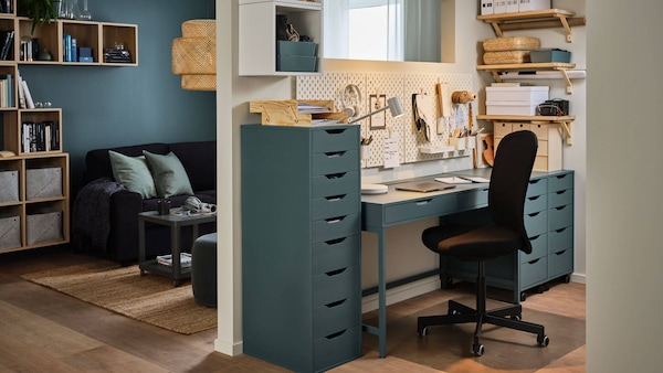 A home workspace with turquoise desk and filing cabinets, with a black swivel chair.