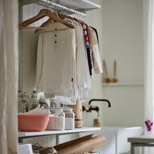 A laundry area with a white BOAXEL storage combination, filled with garments on hangers and laundry accessories.