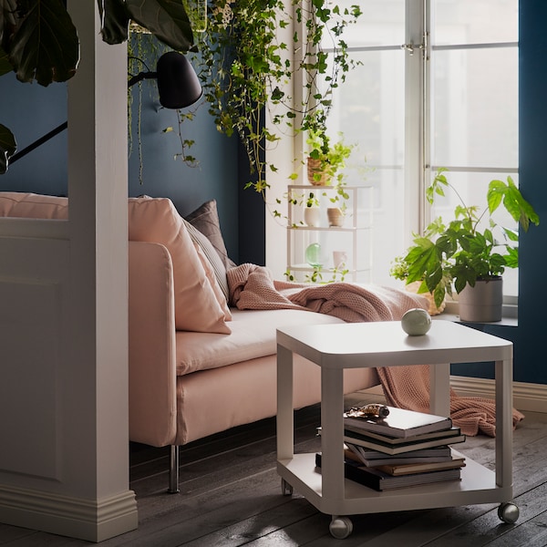 A light pink SÖDERHAMN chaise lounge facing two windows with a TINGBY side table beside it, surrounded by plenty of plants.