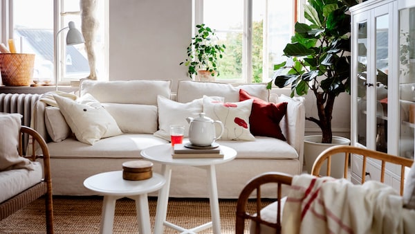 A living room area with a white sofa and white side tables with large windows in the background.