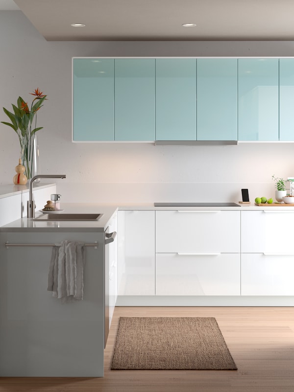 A minimalist kitchen with high-gloss white and light turquoise doors, a sink with a faucet and glass vase with flowers.