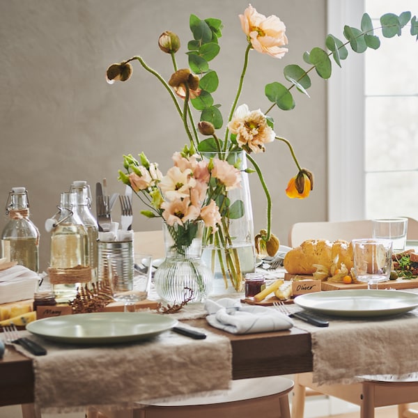 A MÖRBYLÅNGA table festively set with lengths of AINA fabric, FÄRGKLAR plates, flowers in vases and various decorations.