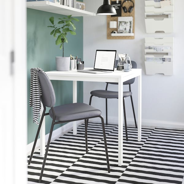 A small dining nook with a white MELLTORP table set up for working from home and two dark grey KARLJAN chairs.