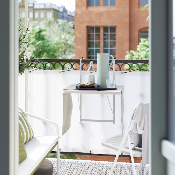 A small white balcony table hung on the balcony rail, with a pitcher, a plate of food and drinks on it.
