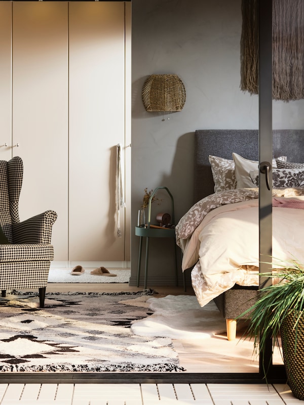A sunny bedroom with a PAX/REINSVOLL wardrobe combination near an IDANÄS bed with a mix of floral and plain bed linen.