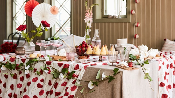 A table set for a party with many items from the ANLEDNING collection including a white/red tablecloth and glasses.