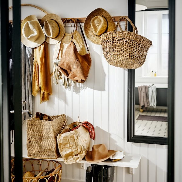 A white hallway with racks with six knobs holding bags, hats and scarves in natural colours, beside a TOFTBYN mirror.