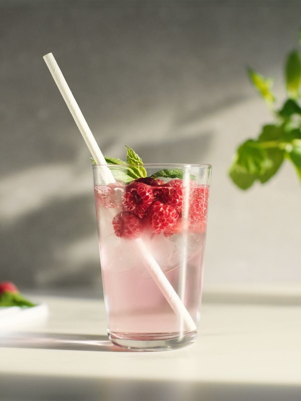 A white paper straw in a glass of water with brightly colored fruits, which change several times through stop-animation.
