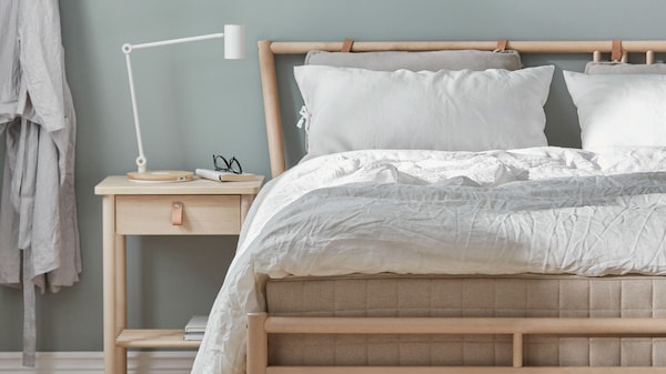 A wooden bed frame with white bedding and a wooden nightstand against a light green wall.
