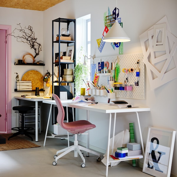 A workspace with a white LAGKAPTEN/TILLSLAG desk, light brown-pink LÅNGFJÄLL office chair, plus white pegboards and pendant.