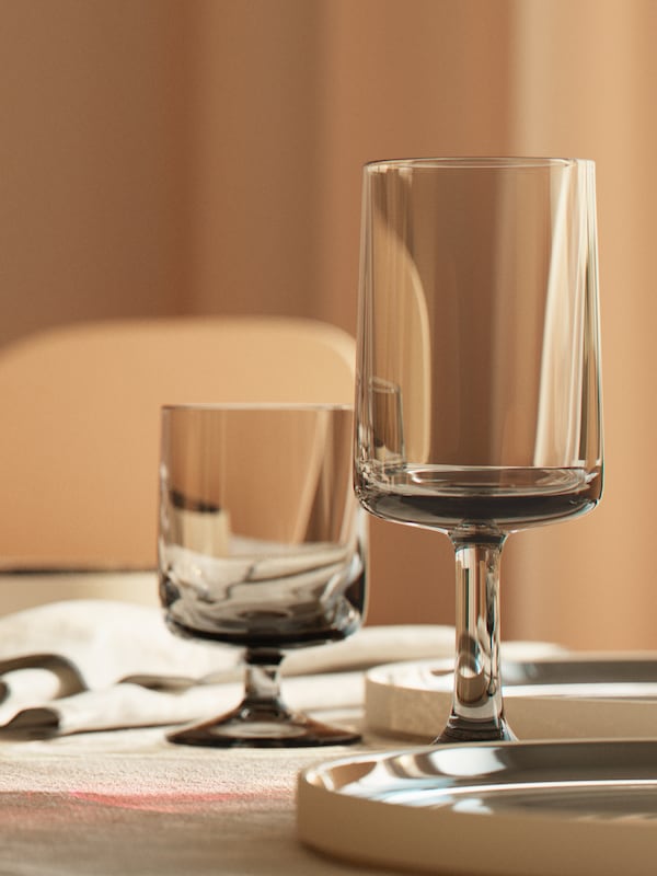 An OMBONAD grey wine glass and goblet are on a table with some OMBONAD napkins and plates.