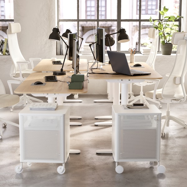 An open office space with four desks, four office chairs, four work lamps and two drawer units.