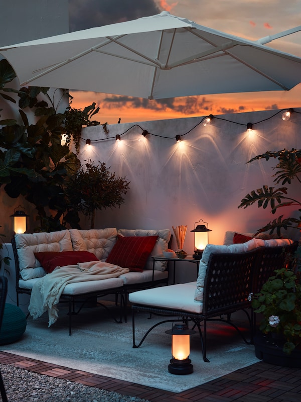 An outdoor area with two modular corner sofas, a white parasol, lighting chains and three lanterns.