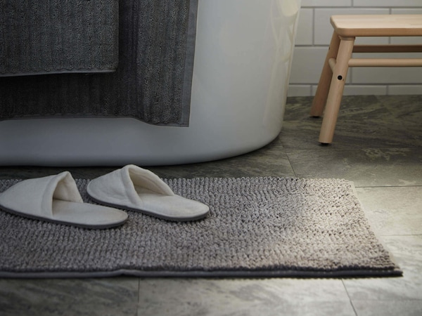 Bathroom bath mat with slippers by the shower and a bathroom stool.