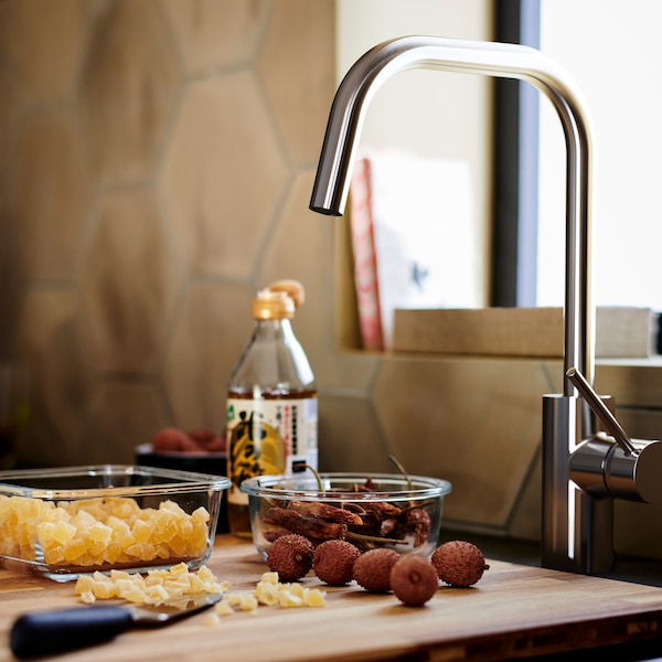 Brown wood chopping board with two glass containers, beneath an ÄLMAREN kitchen mixer faucet in stainless steel colour.