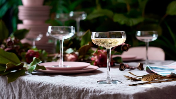 Champagne glasses holding bubbly on dinner table with linen table cloth, pink platerware & floral decorations. 