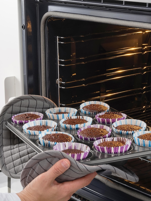 Cupcakes in a cupcake tin being removed from the oven with oven towels.