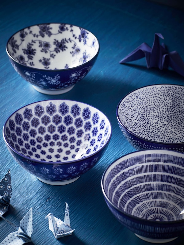 Decorative stoneware and ceramic plateware bowls in blue and white on a blue table. 