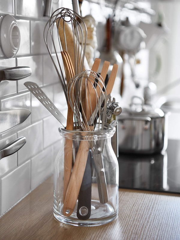 Glass vase holding kitchen utensils on kitchen counter. 