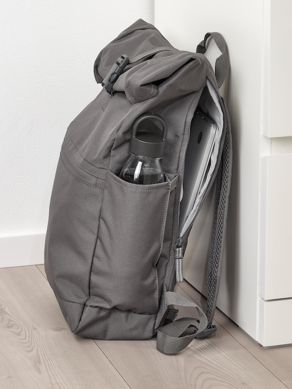 Gray backpack with water bottle on floor next to set of drawers. 
