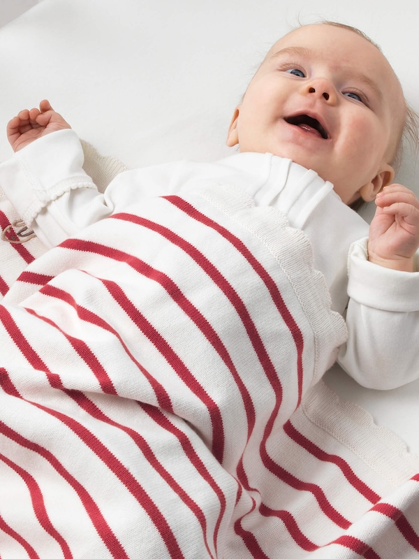 Infant wrapped in white baby blanket with red stripes. 