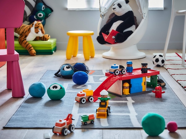 Kids toys on playmat next to color plastic kids furniture. 