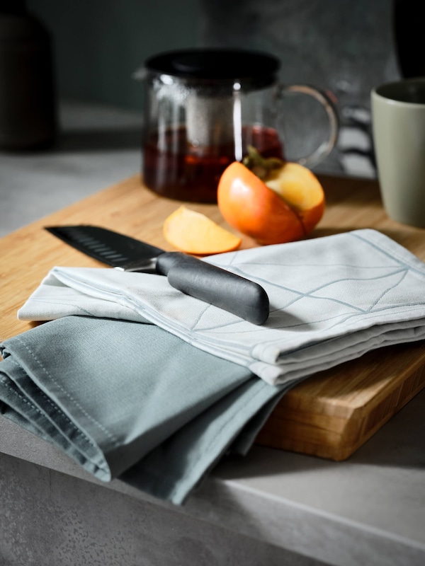 Kitchen knife, clothe napkins & glass teapot on wooden cutting board. 