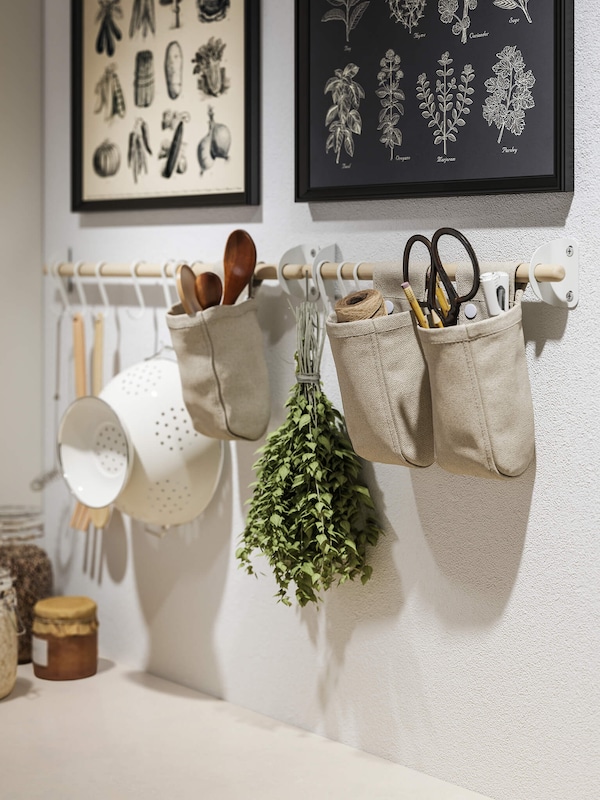 Kitchen utensils hanging from kitchen rack below modern decor style wall art featuring plant illustrations. 