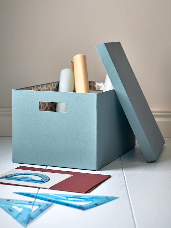 Light blue storage box with rolled up papers & protractors on the floor.