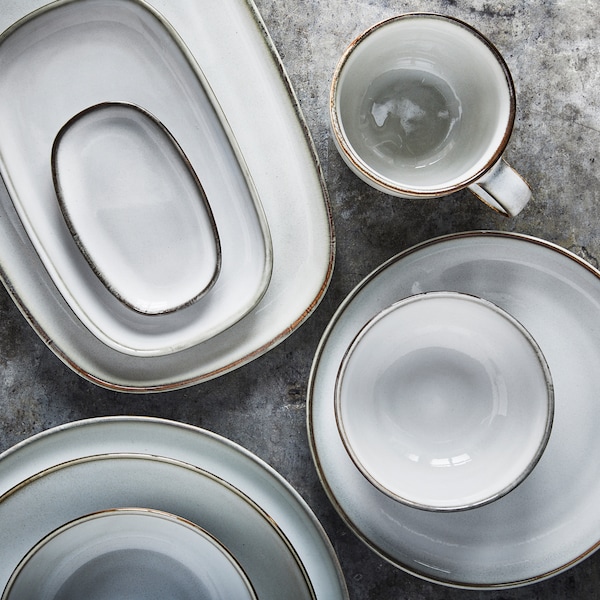 Light grey bowls, plates and serveware in three piles with a cup beside them on a grey surface.