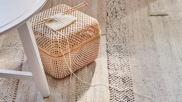 Low pile woven rug with knitting basket & knitting needle by a white circular table. 