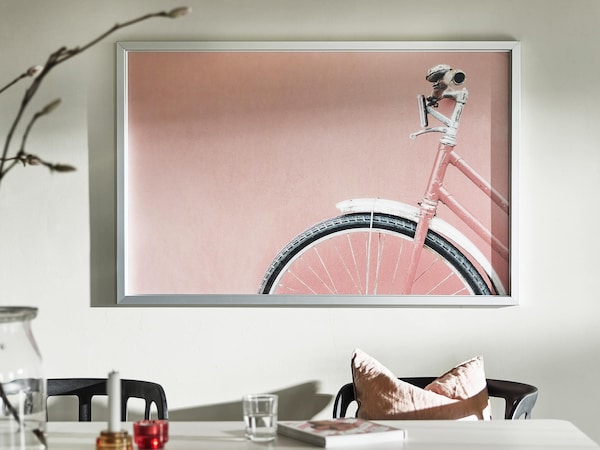 Modern wall art featuring a pink bike in trim metal frame before a minimalist table setting. 