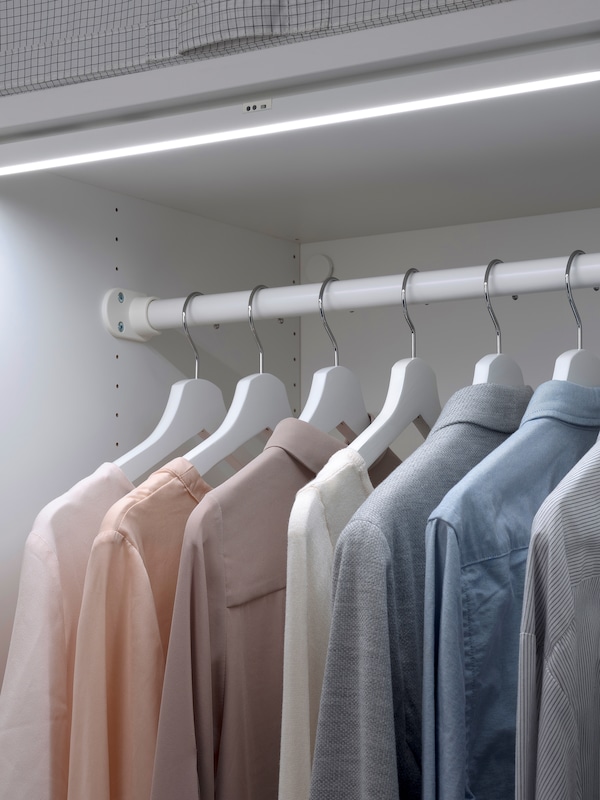 Shirts hanging by coat hangers from a rail in a white storage unit, with integrated lighting.