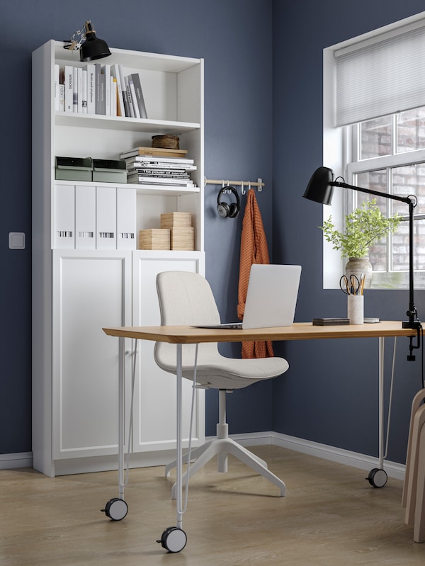 A workspace at home with dark blue walls, an ANFALLARE/KRILLE desk, a LÅNGFJÄLL conference chair and a BILLY bookcase.