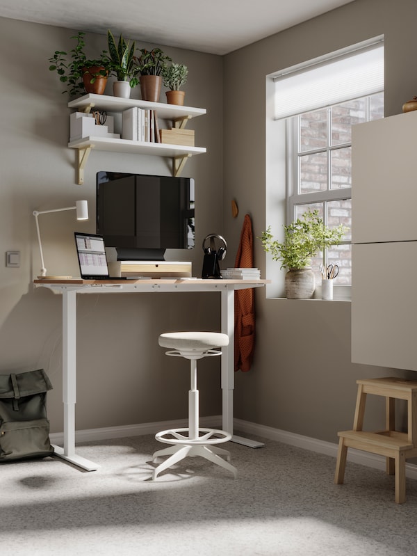 A workspace at home with beige walls, a SKARSTA sit/stand desk, LIDKULLEN active sit/stand support and BESTÅ storage units.